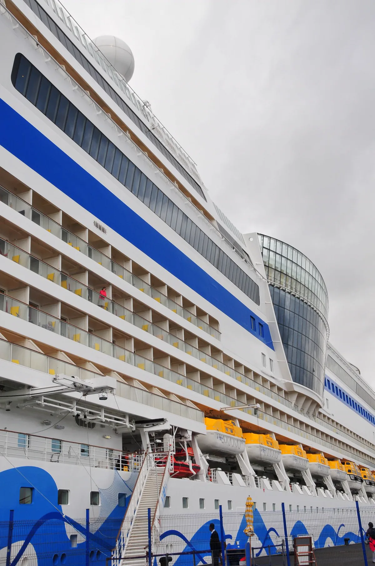Kreuzfahrtschiff mit sichtbaren Balkonkabinen und Rettungsbooten im Hafen
