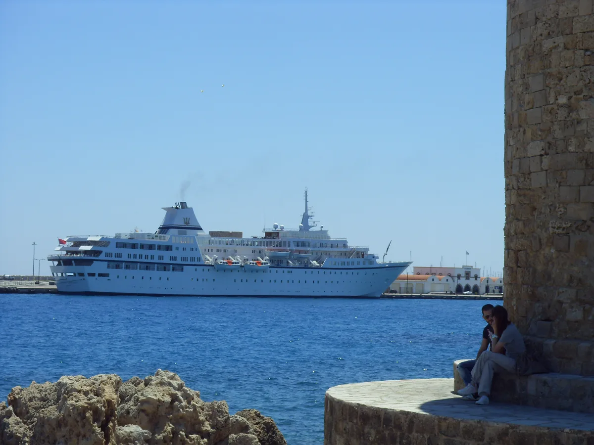 Paar sitzt am Hafen von Rhodos mit Blick auf ein Kreuzfahrtschiff