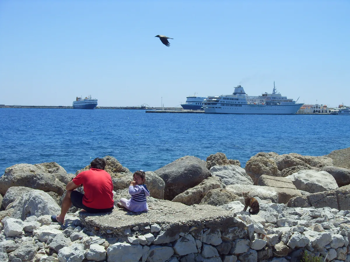 Erwachsener und Kind am Hafen von Rhodos mit Kreuzfahrtschiffen im Hintergrund